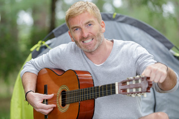 mature man tuning guitar by his tent