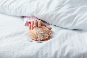Young woman reaching hand for tasty bun while lying in bed