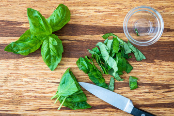 Fresh basil with a paring knife on a rustic grove bamboo cutting board, small glass bowl