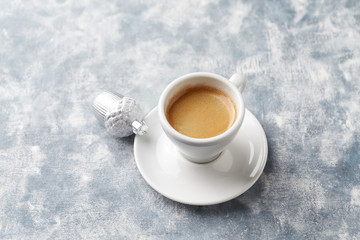 Cup of coffee and silver Christmas bauble on bright wooden background. Copy space.