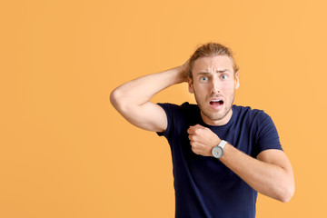 Stressed man with watch on color background
