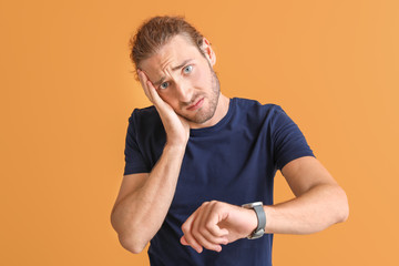 Stressed man with watch on color background
