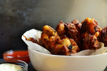 Fried chicken wings. Chicken wings on a dark background. Barbecue meat, grill. Sauce in bowls, ketchup, mayonnaise, mustard, cheese sauce. Appetizing fried meat in the white plate. bowl.