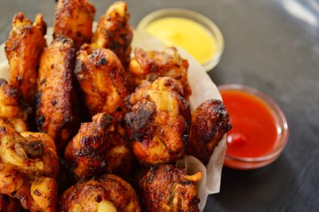 Fried chicken wings. Chicken wings on a dark background. Barbecue meat, grill. Sauce in bowls, ketchup, mayonnaise, mustard, cheese sauce. Appetizing fried meat in the white plate. bowl.