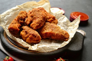 Appetizing food on a black dark table background. Chicken nuggets on parchment. Nuggets on a wooden board. Fried chicken fillet.
