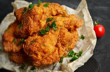 Appetizing food on a black dark table background. Chicken nuggets on parchment. Nuggets on a wooden board. Fried chicken fillet.
