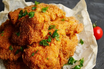 Appetizing food on a black dark table background. Chicken nuggets on parchment. Nuggets on a wooden board. Fried chicken fillet.
