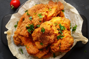 Appetizing food on a black dark table background. Chicken nuggets on parchment. Nuggets on a wooden board. Fried chicken fillet.