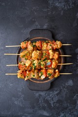 Appetizing food on a dark background. Chicken skewers with mushrooms and tomato. Oven skewered chicken fillet. Chicken kebab on the wooden board and black plate.