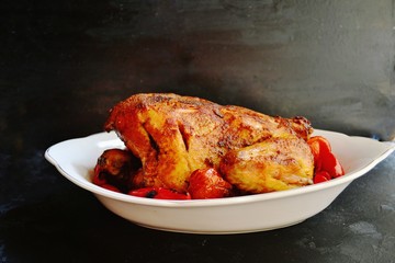 Baked whole chicken.  Appetizing whole chicken in the white plate on a dark concrete table background. Festive, Christmas dish.