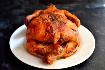 Baked whole chicken. Appetizing whole chicken with a crispy golden crust on a dark concrete table background. Festive, Christmas dish.