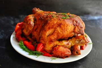 Baked whole chicken.  Appetizing whole chicken in the white plate on a dark concrete table background. Festive, Christmas dish.