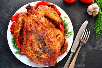 Baked whole chicken.  Appetizing whole chicken in the white plate on a dark concrete table background. Festive, Christmas dish.