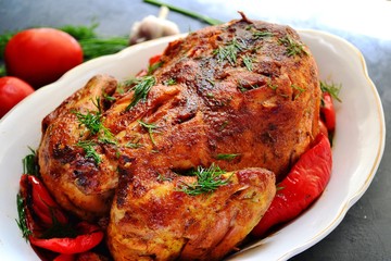 Baked whole chicken.  Appetizing whole chicken in the white plate on a dark concrete table background. Festive, Christmas dish.