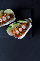 Oyster shell with seafood salad and lime on dark background