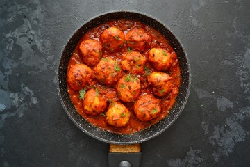 Meatballs in tomato sauce. Chicken meatballs. Meatballs in a pan on a dark table background isolated.