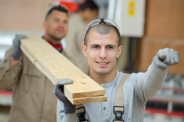 two men carrying planks of wood together on their shoulders