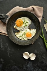 Tasty breakfast. Food on the table. Food on a dark concrete background. Fried eggs in a pan. Eggs, green onions, brown bread, cucumbers.