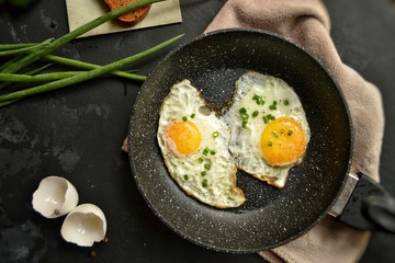 Tasty breakfast. Food on the table. Food on a dark concrete background. Fried eggs in a pan. Eggs, green onions, brown bread, cucumbers.