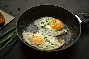 Tasty breakfast. Food on the table. Food on a dark concrete background. Fried eggs in a pan. Eggs, green onions, brown bread, cucumbers.