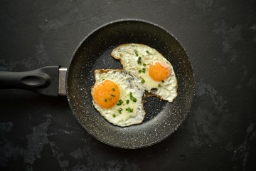 Tasty breakfast. Food on the table. Food on a dark concrete background. Fried eggs in a pan. Eggs, green onions, brown bread, cucumbers.