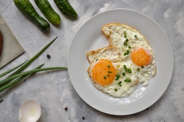 Tasty breakfast. Food on the table. Food on a light gray decorative background. Fried eggs in a white plate. Eggs, green onions, brown bread, cucumbers.