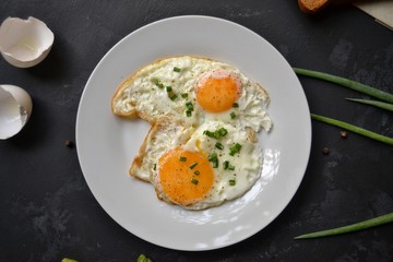 Tasty breakfast. Food on the table. Food on a black concrete decorative background. Fried eggs in a white plate. Eggs, green onions, brown bread, cucumbers.