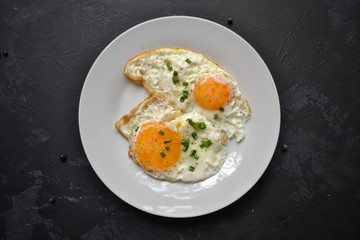 Tasty breakfast. Food on the table. Food on a black concrete decorative background. Fried eggs in a white plate. Eggs, green onions, brown bread, cucumbers.