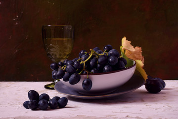 Still life with black grapes and white wine in a green glass, plums.