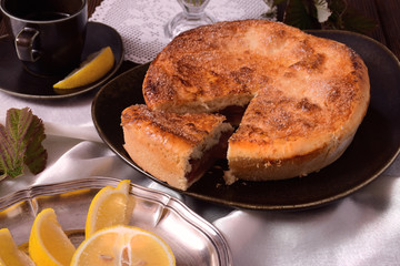 Closed cake on a brown plate of unusual shape. Lemons slices on a silver plate.