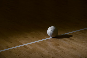 Volleyball On Hardwood Court Floor With Spot Lighting