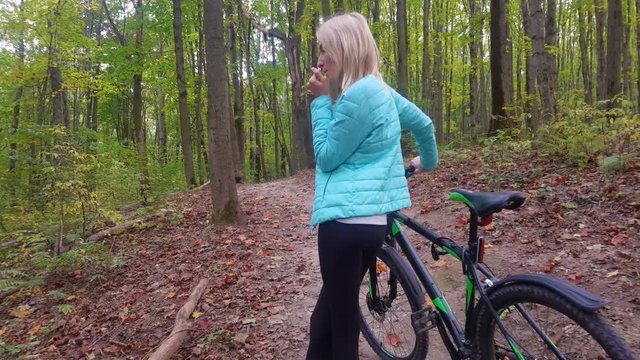 woman on bicycle in forest. Rubs his palms and blows on them. cold, frozen.