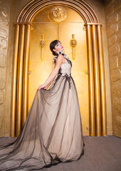 Naklejka premium alluring sexy full length woman in evening dress posing over golden studio background
