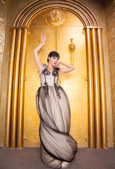 Naklejka premium alluring sexy full length woman in evening dress posing over golden studio background