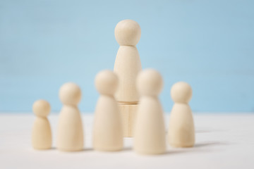Wooden figures of man on toy block and people before him.