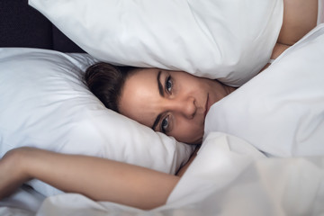 Young stressed woman can not sleep and covers her head and ears with pillow.
