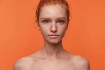 Foto op Canvas Studio photo of beautiful young readhead female with casual hairstyle standing over orange background without clothes, looking at camera with calm face © timtimphoto