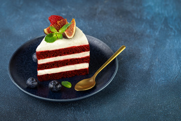A piece of delicious red velvet cake on a blue plate on dark background.