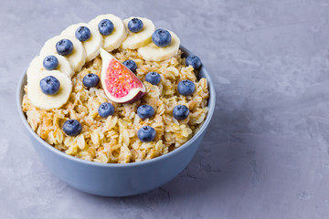 Healthy breakfast. Oatmeal with blueberries, banana and figs. Oatmeal with fruits and berries in a bowl. Cooked oatmeal on cement background. Copy space