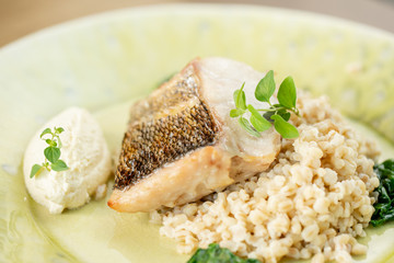 Roasted pike perch or cod fish with bulgur. Dish decorated with a spinach. Restaurant menu