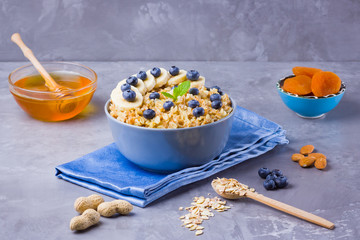 Oatmeal with berries and nuts. Breakfast: oatmeal, blueberries, banana and honey. Cooked oatmeal in bowl on blue napkin