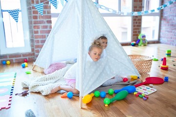 Beautiful toddlers playing inside tipi over blanket around lots of toys at kindergarten
