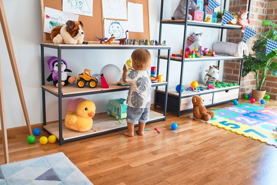 Adorable toddler holding feeding bottle around lots of toys at kindergarten
