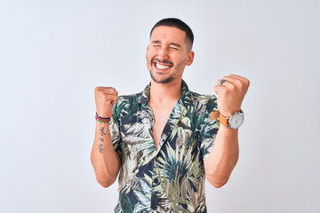 Young handsome man wearing Hawaiian summer shirt over isolated background very happy and excited doing winner gesture with arms raised, smiling and screaming for success. Celebration concept.