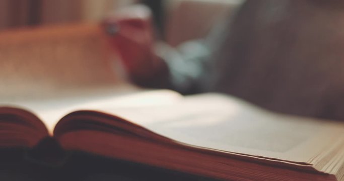 Hand Turning Pages of a Book, CLOSE UP. SLOW MOTION. Unrecognizable Person's Hand reading a book and holding fingers along the lines. Cinematic light at home or library. 