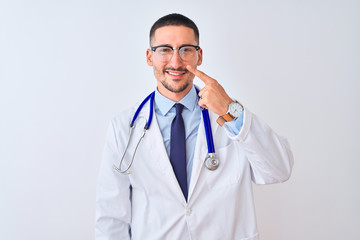 Young doctor man wearing stethoscope over isolated background Pointing with hand finger to face and nose, smiling cheerful. Beauty concept