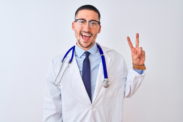 Young doctor man wearing stethoscope over isolated background smiling with happy face winking at the camera doing victory sign with fingers. Number two.