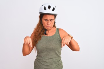 Middle age mature cyclist woman wearing safety helmet over isolated background Pointing down looking sad and upset, indicating direction with fingers, unhappy and depressed.
