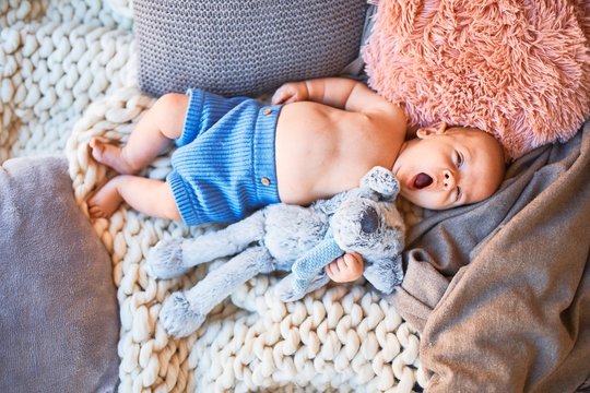 Adorable baby lying down on the sofa over blanket at home. Newborn relaxing and resting comfortable with doll