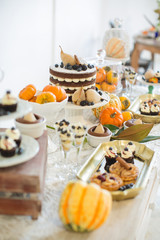 Sweet table. Halloween Wedding Luxor Decor. Chocolate cake with blackberries, blueberries, pears and cinnamon sticks. Cupcakes and tartlets with berries. Surrounded by orange pumpkins
